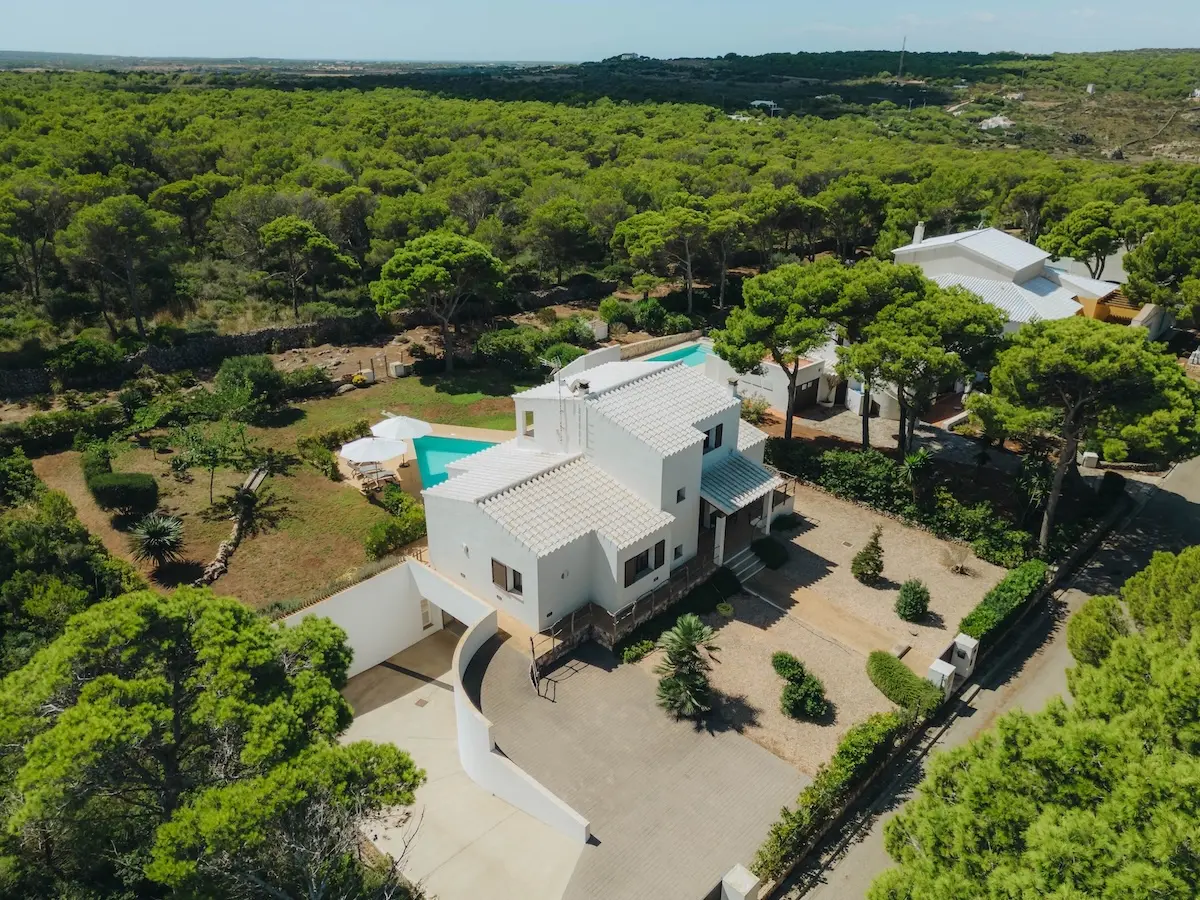Vista aérea frontal de Villa Arrow en Menorca, destacando su piscina de diseño en forma de flecha, terraza con tumbonas y vistas panorámicas al mar Mediterráneo.