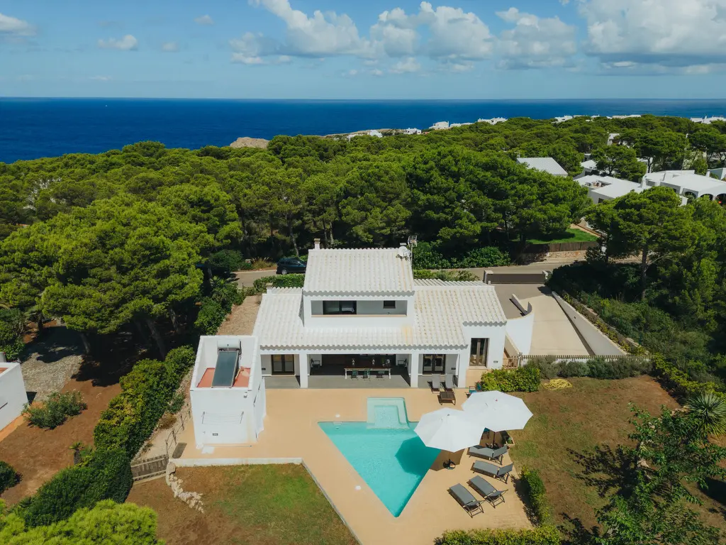 Frontal aerial view of Villa Arrow in Menorca, featuring its unique arrow-shaped swimming pool, sun terrace, and panoramic views of the Mediterranean Sea.