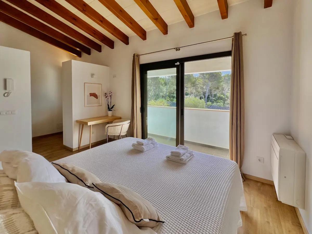 Bedroom view at Villa Arrow showing a minimalist wooden desk and chair setup next to large glass doors that offer a scenic view of the surrounding trees.