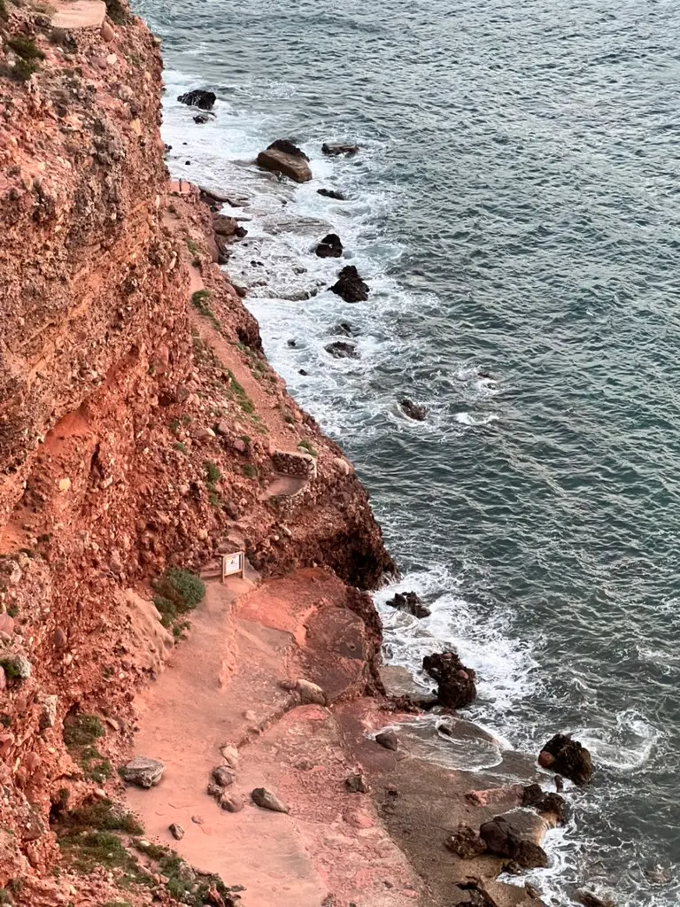 Dramatic red-toned rocky cliffs meeting the deep blue Mediterranean Sea along the coastline of northern Menorca.