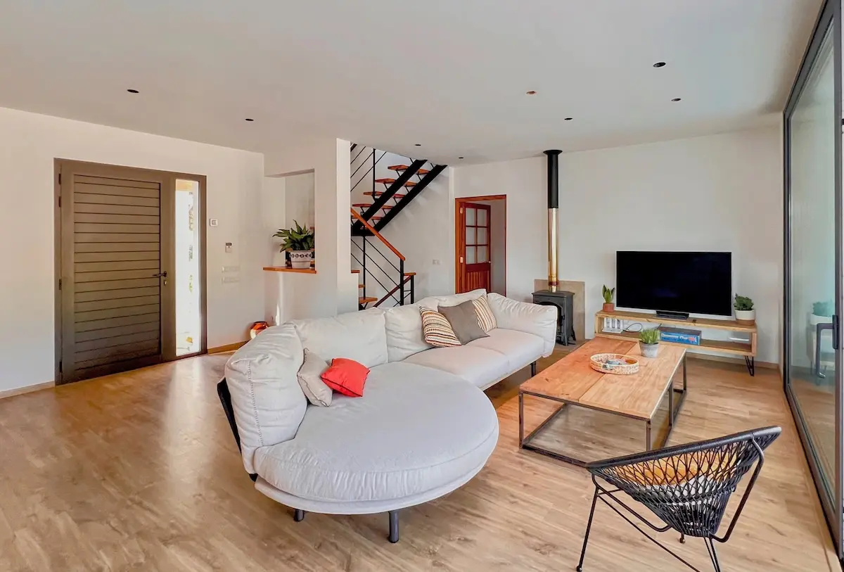 Contemporary living room at Villa Arrow featuring a large white sectional sofa, a minimalist wooden coffee table, a wood-burning stove, and a stylish black metal staircase with wooden steps