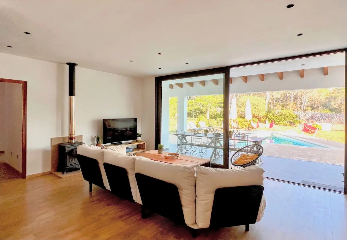 View from the living room of Villa Arrow looking out through large sliding glass doors to the outdoor dining patio, swimming pool, and sun-drenched garden.
